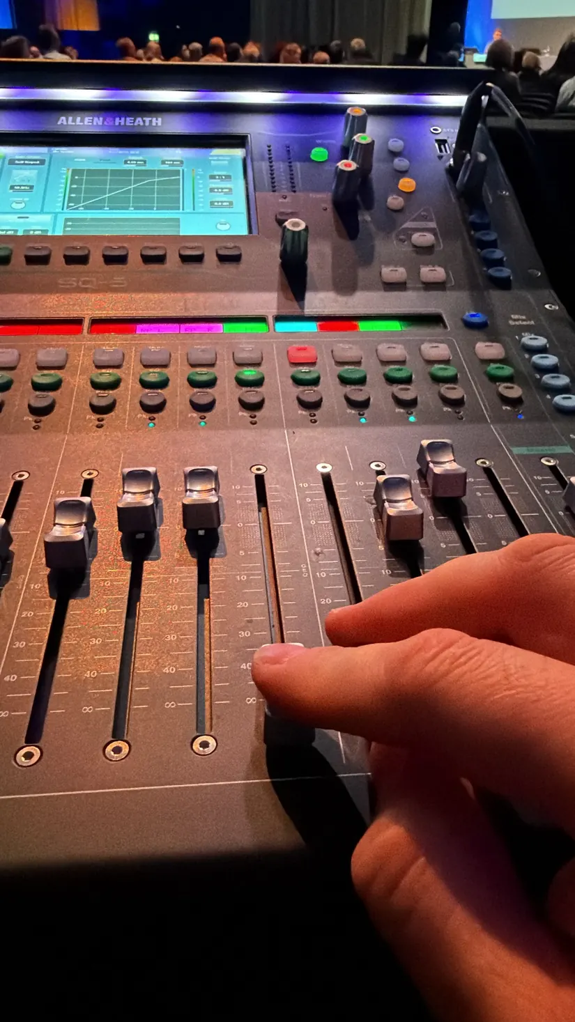 Hand eines Tontechnikers an den Fadern eines Digitalmischpults