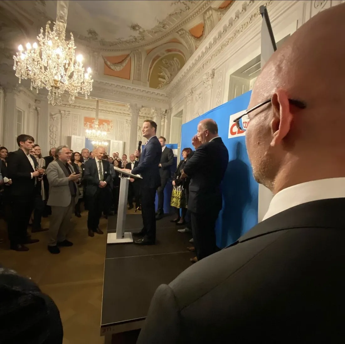 Rede vor Publikum in einem Saal mit Kronleuchter