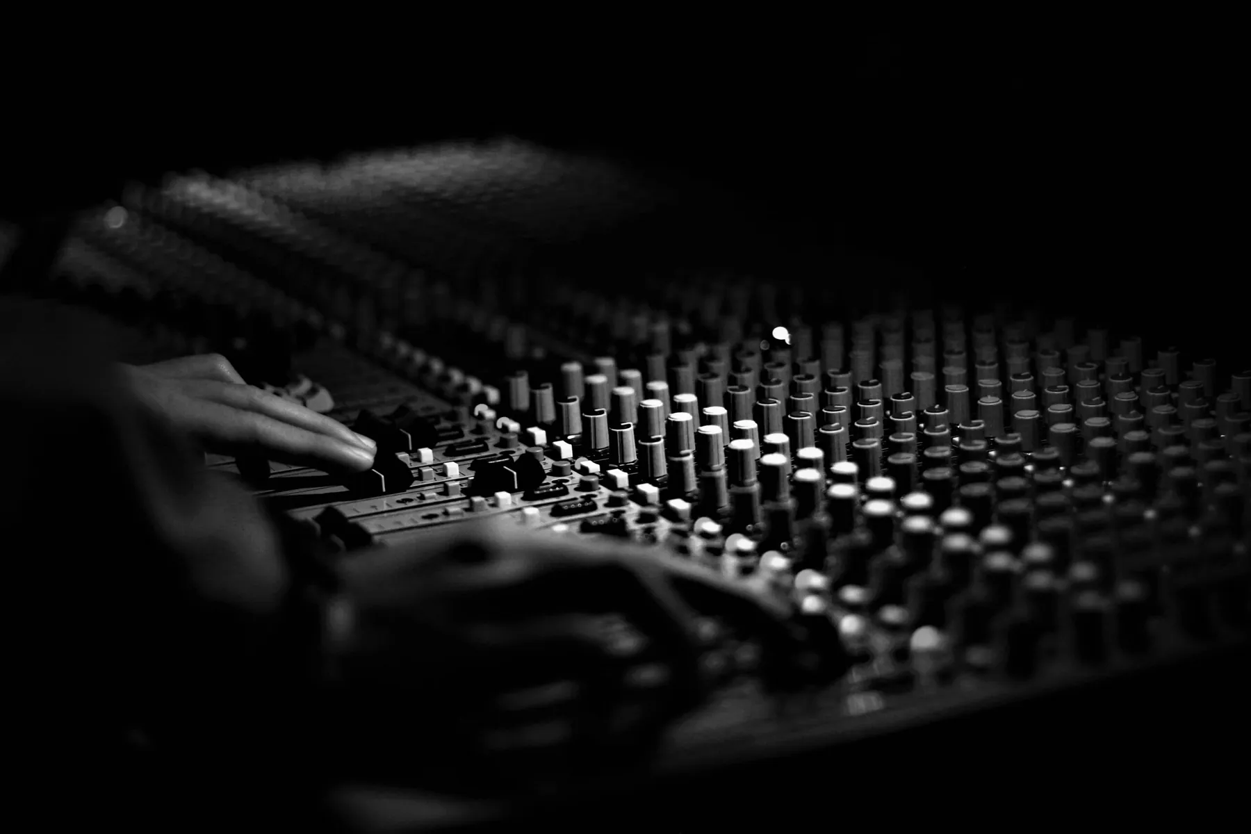 Hände an den Reglern eines großen analogen Mischpults, schwarz-weiß