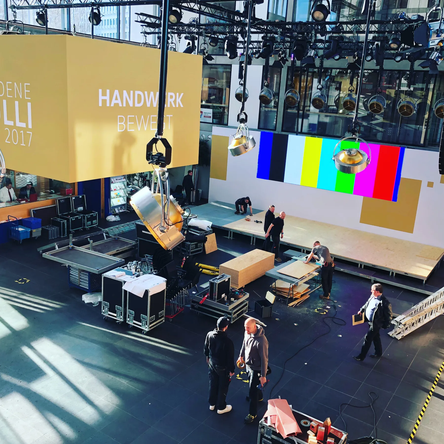 Aufbau in einer Halle: Traversen, Scheinwerfer und LED-Wand mit Testbild, Techniker bei der Arbeit